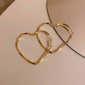Close-up detail of golden heart-shaped twisted hoop earrings on a light background