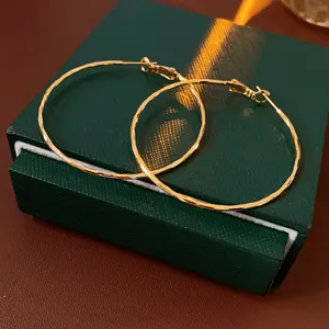 Elegant large gold hammered hoop earrings displayed on a luxury dark green jewelry box