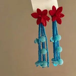 Gedetailleerd overzicht van rode viltbloem oorbellen met lange blauwe kralenkwasten