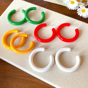 Close-up of colorful acrylic C-shaped hoop earrings in green, red, yellow, and white
