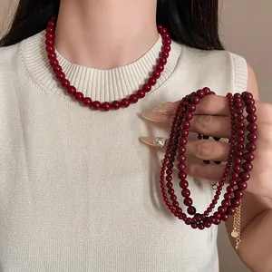 Detail einer tiefroten Glasperlenkette am Model mit cremefarbener Weste