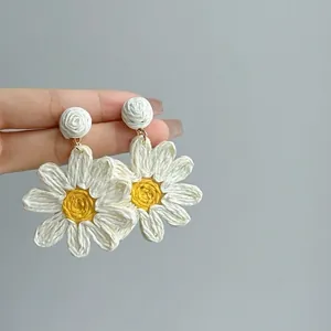 Detail view of handmade woven daisy drop earrings with white petals and yellow center.