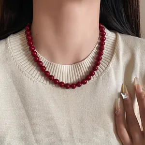 Elegante Retro-Halskette mit roten Glasperlen, getragen von Model im beigen Stricktop
