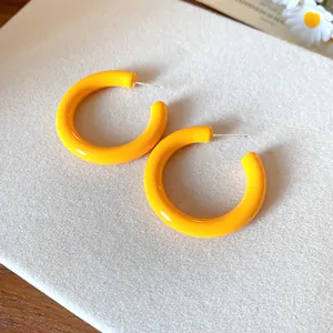 Close-up of bright yellow C-shaped acrylic earrings on a textured white surface