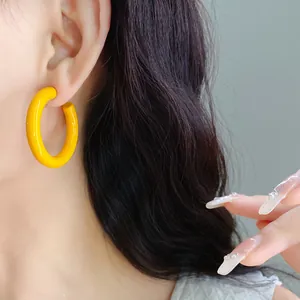 Close-up of a bright yellow C-shaped acrylic hoop earring worn on a model's ear