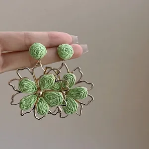 Close-up of green woven flower earrings with gold metal frame detailing.