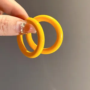 Close-up of bright yellow C-shaped acrylic hoop earrings held by hand