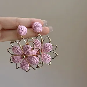 Close-up of pink woven flower earrings with gold metal frame accents