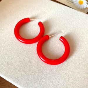 Close-up of vibrant red acrylic C-shaped hoop earrings with silver pins on a beige display pad.