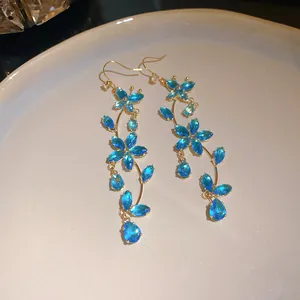 Detailed shot of sparkling blue zircon butterfly and flower tassel hook earrings in gold.
