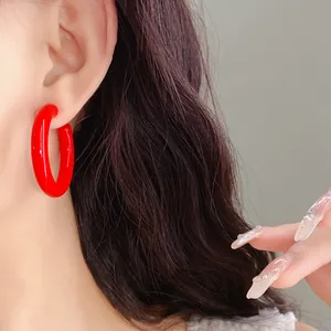 Detailed close-up showing a vibrant red acrylic C-shaped hoop earring worn on an ear
