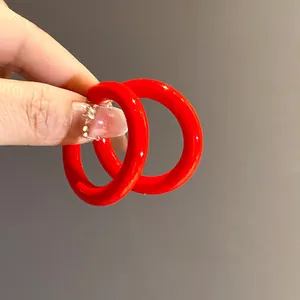 Close-up detail of vibrant red acrylic C-shaped hoop earrings held by hand for scale