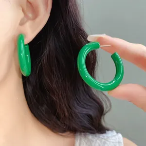 Detail showing green acrylic C-shaped earrings being worn and held by hand