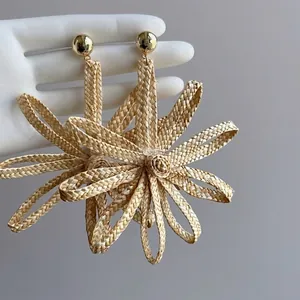Close-up of woven straw flower earrings with golden studs in bohemian vacation style.