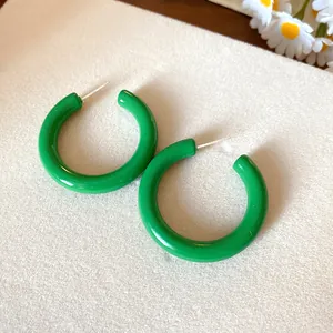 Macro view of vibrant green acrylic C-shaped earrings with silver needles on cream felt surface