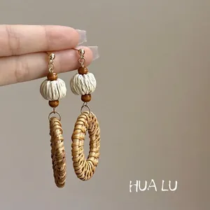 Close-up of bohemian woven rattan hoop earrings with wood beads and textured ball.