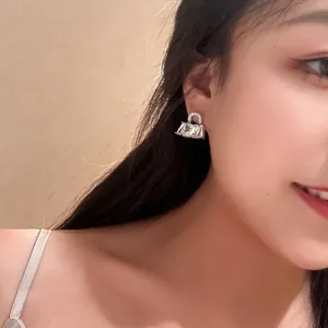 Detail view of sparkling handbag-shaped stud earrings worn by a model
