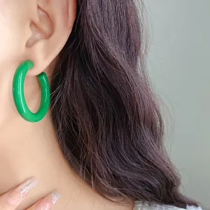 Detailed close-up of vibrant green C-shaped acrylic hoop earrings worn by an Asian model