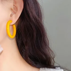 Close-up of dopamine yellow acrylic C-shaped hoop earring on model's ear.