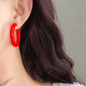 Close-up view of vibrant red acrylic C-shaped hoop earrings worn by a model for detail