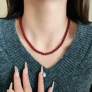 Detailansicht einer roten Glasperlenkette am Hals getragen über grünem Pullover