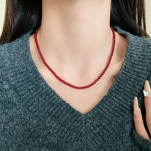 Nahaufnahme einer roten Glaskugelhalskette im Retro-Stil an einem Modell mit grauem Pulli.