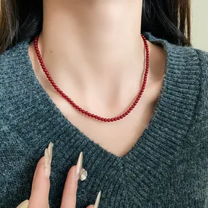 Elegante Nahaufnahme einer roten Perlenkette im Retro-Stil am Hals eines Models im grauen Pullover.