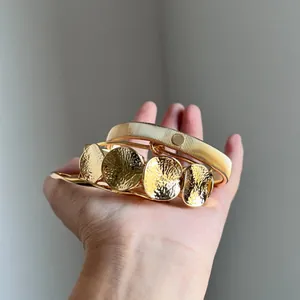 Set mit vier goldfarbenen, unregelmäßigen Armreifen mit strukturierten Rundplatten