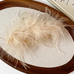 Elegant ostrich feather hair claw clip with cream fluffy texture on a minimalist tray