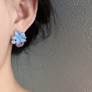 Close-up detail of an elegant blue flower earring with a pink crystal worn on a model's ear