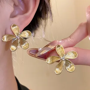Close-up of golden flower stud earrings showing textured petals and silver needle detail