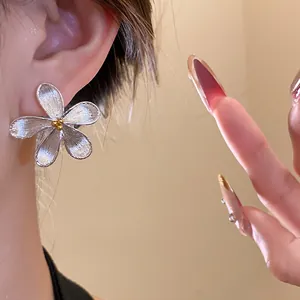 Macro detail of silver flower stud earrings with brushed metal petals and gold center