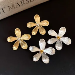 Macro view showing the fine brushed metal texture of gold and silver flower stud earrings