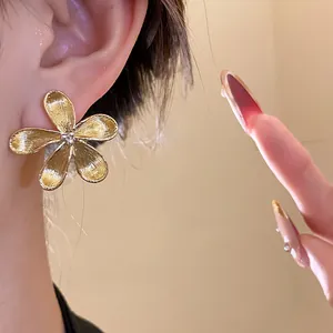 Close-up detail of elegant gold flower stud earring with textured metal finish petals