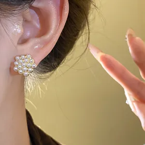 Close-up detail of a hexagonal gold earring with small pearls worn on an Asian woman's ear.