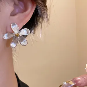 Close-up view of minimalist silver flower stud earrings with textured petals on ear