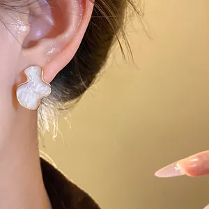 Detail of gold-edged pearlescent geometric stud earring on model with warm lighting
