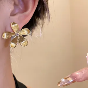 Close-up of golden flower stud earring with brushed metal texture on ear