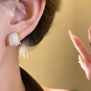 Close-up detail of a geometric gold-rimmed stud earring with white cat's eye stone