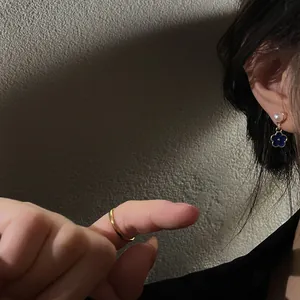 Primo piano dettagliato di un orecchino a fiore in smalto blu con perla sul lobo.