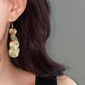 Primo piano di eleganti orecchini pendenti tondi in oro opaco su una modella asiatica