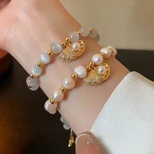 Elegant gold-plated cat's eye and pearl bracelets with crystal shell charms on wrist.