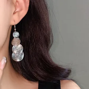 Dettaglio di orecchini a cerchio irregolari in argento con finitura glitterata.