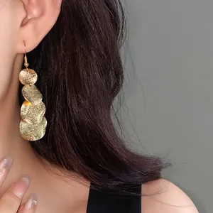 Primo piano di orecchini a pendente con dischi dorati opachi su modella