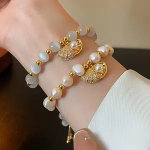 Detail view of pearl and cat-eye stone bracelets with gold shell pendants on wrist