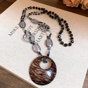 Dettaglio di una collana bohémien in resina con ciondolo ovale leopardato e perle nere chic.