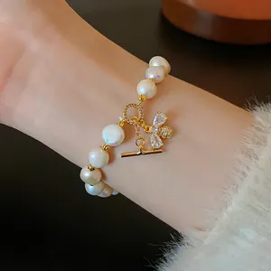 Close-up of a gold-plated pearl bracelet featuring a sparkling zircon bee charm and OT clasp