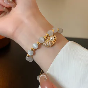 Detailed view of a gold-plated shell charm bracelet with pearls and cat's eye beads