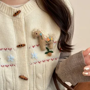 Dettaglio di una graziosa spilla poney in tessuto ricamato su un cardigan bianco