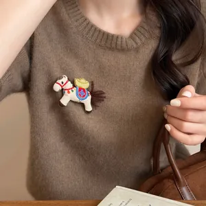 Dettaglio di una spilla a forma di cavallo in tessuto su un maglione di maglia marrone